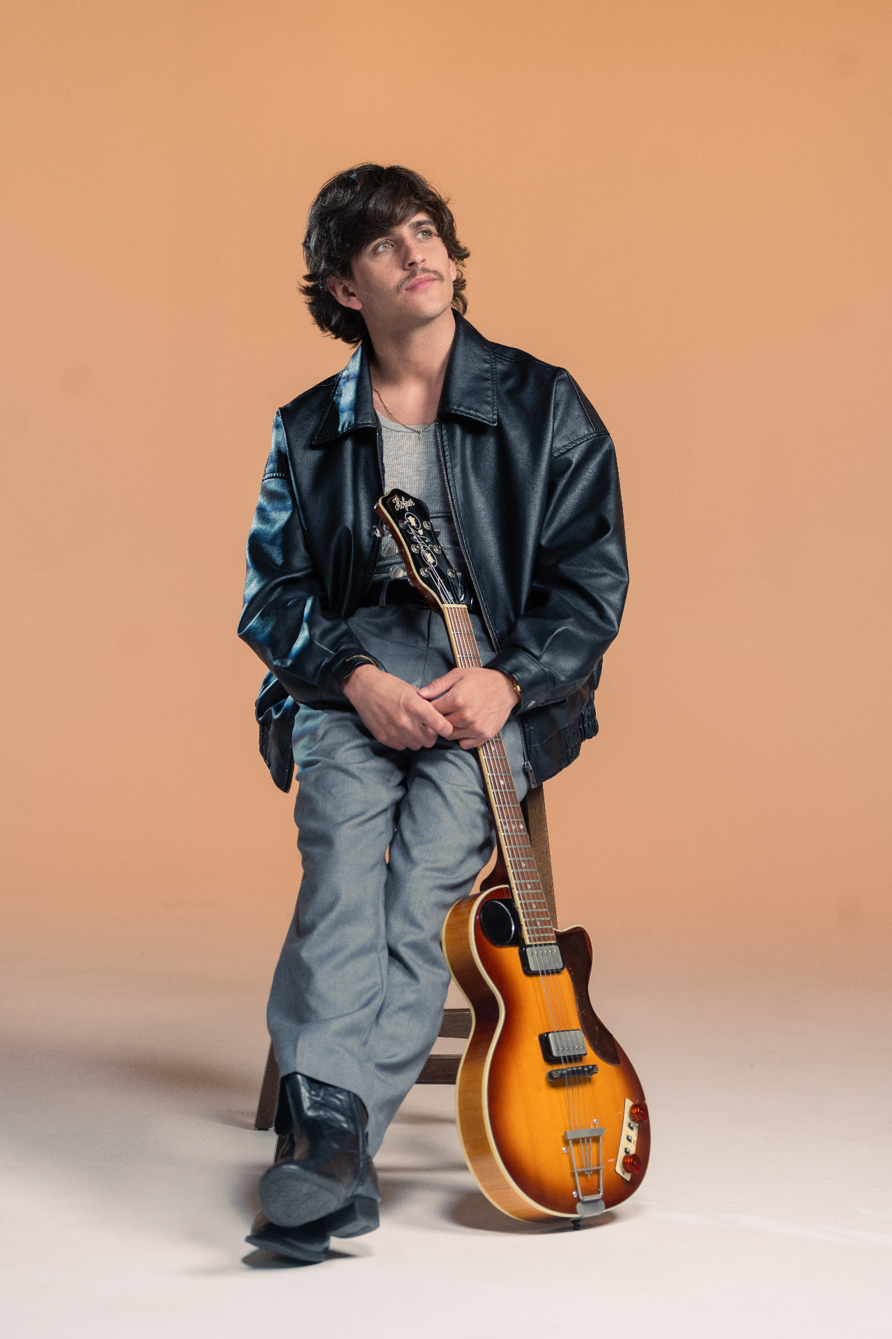 Montalvo con guitarra Höfner y chaqueta de cuero, fondo naranja